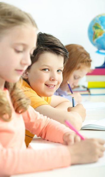 Portrait of smart schoolboy looking at camera between classmates