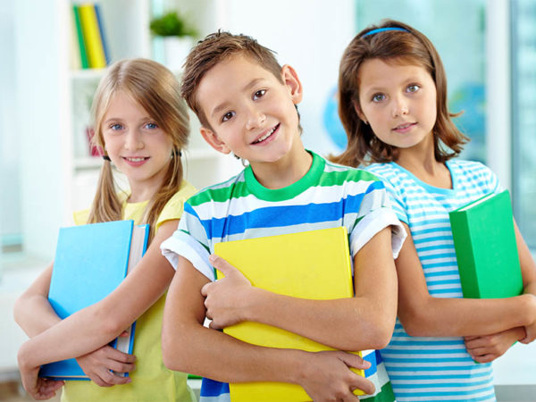 Portrait of happy classmates with books looking at camera in classroom